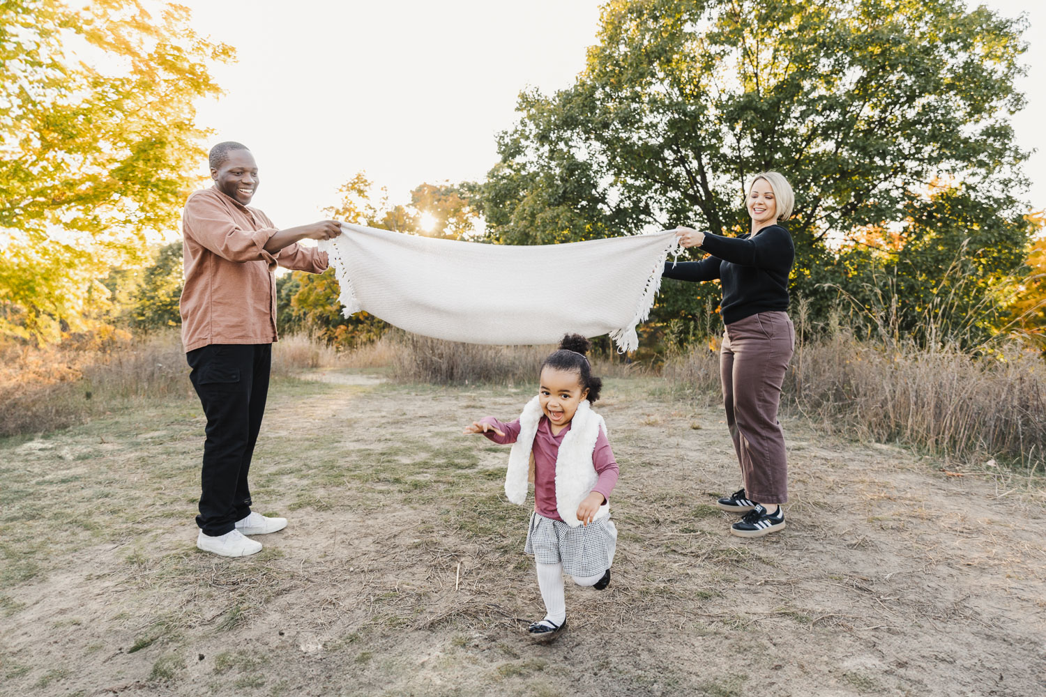 Preschool age girl running under blanket help up by her parents at High Park