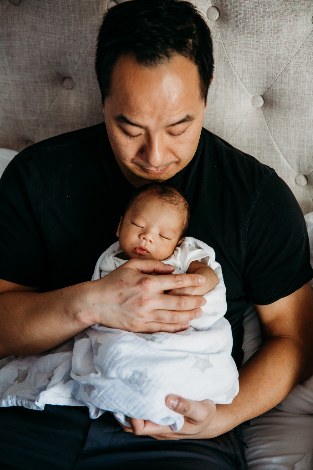 Father holding sleeping newborn son on bed