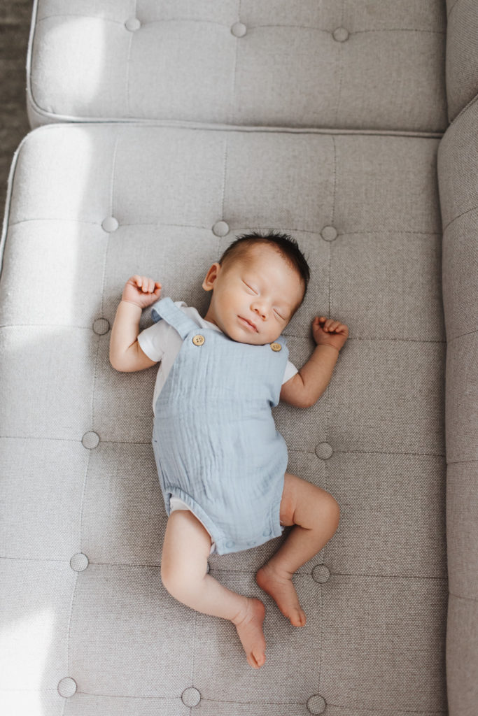 Baby Stores Toronto - Sleeping newborn boy in blue overalls on grey couch
