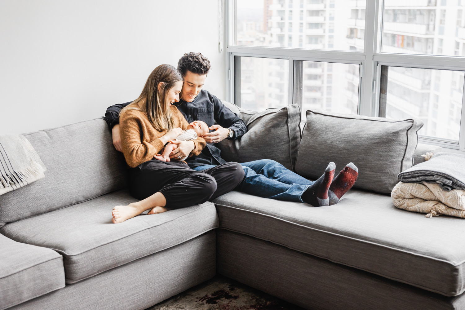 Parents hanging out with newborn son on grey living room couch