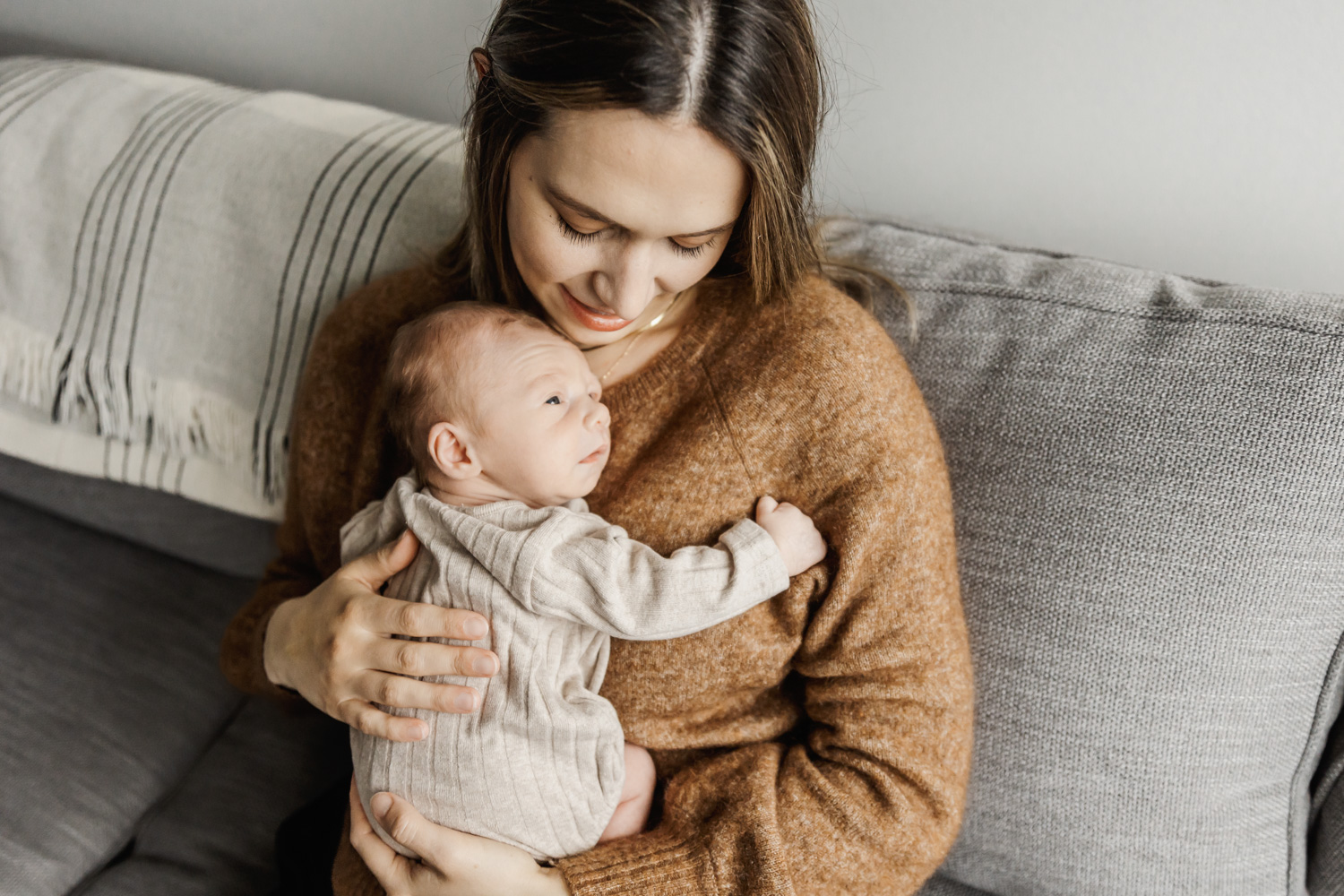Mom in brown sweater cuddling with newborn baby boy on living room couch