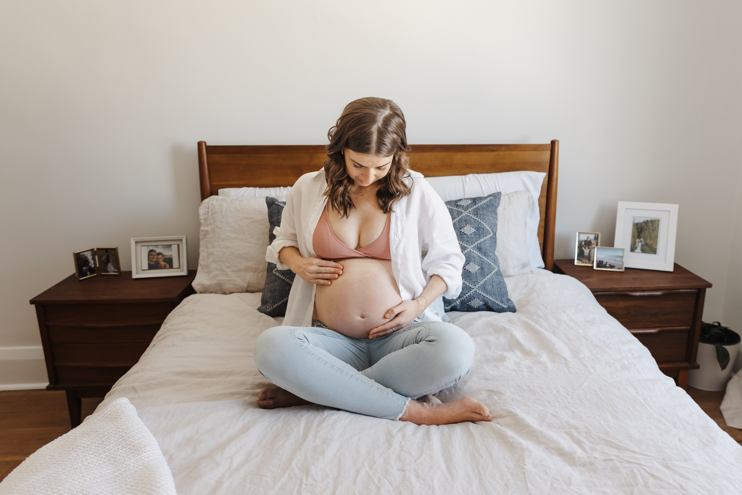 Expecting mom sitting cross legged on bed while looking at her belly. Midwife Alliance