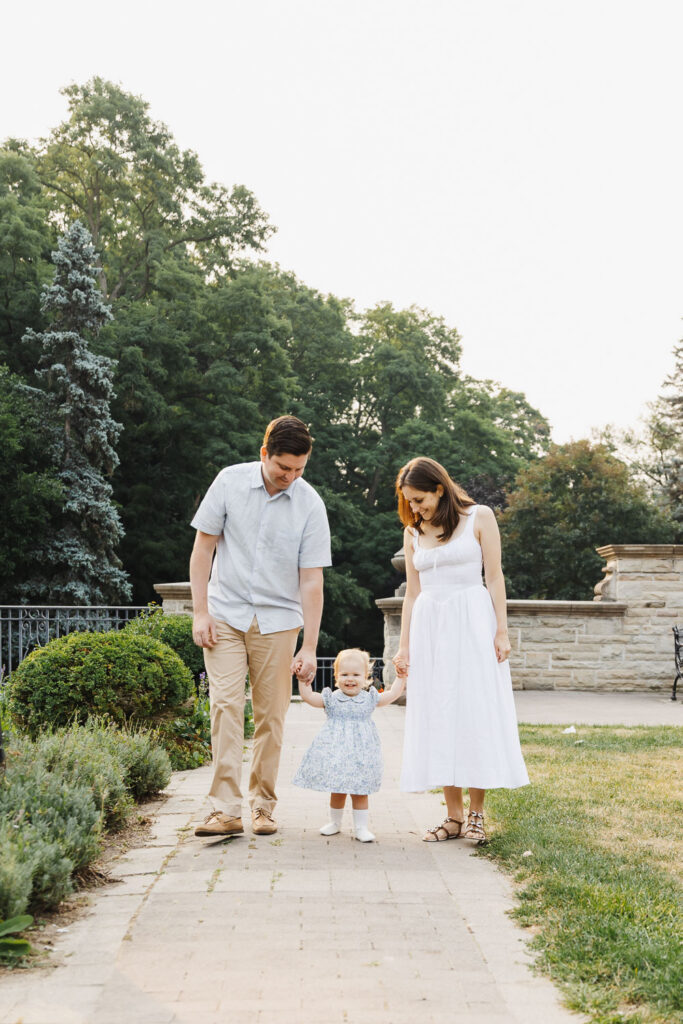 Summer Family Photos at Alexander Muir Memorial Gardens 8 Parents and one year old daughter walking on path at Alexander Muir Memorial Gardens during their family photo session by Claire Binks Photography