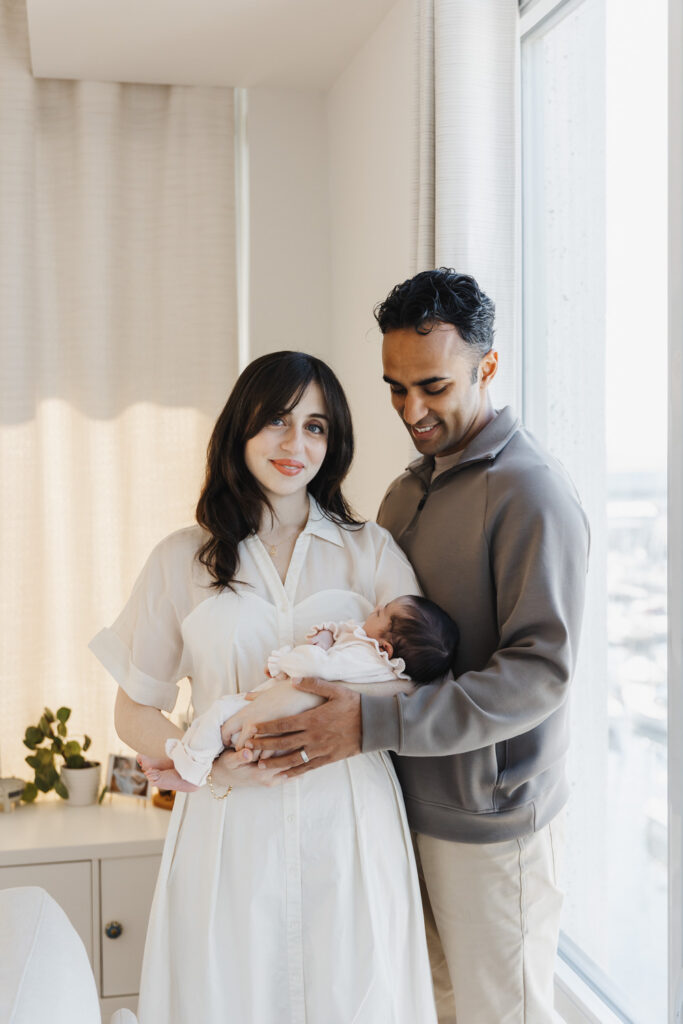Parents holding newborn in bright living room of downtown Toronto condo during their in-home newborn photo session