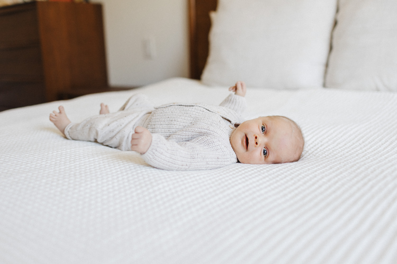 bright eyed newborn boy laying on white bed captured in a bright Toronto bedroom