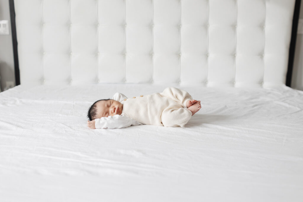 Newborn baby boy dressed in cream knit overalls on bed