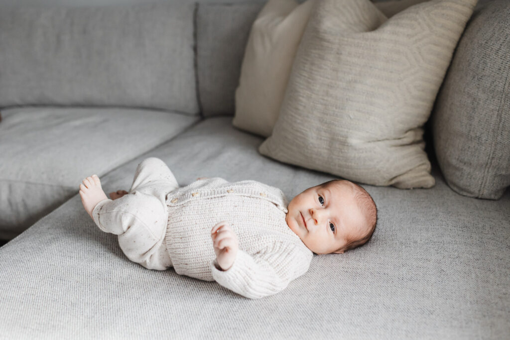 newborn boy dressed in knit outfit laying on a grey couch