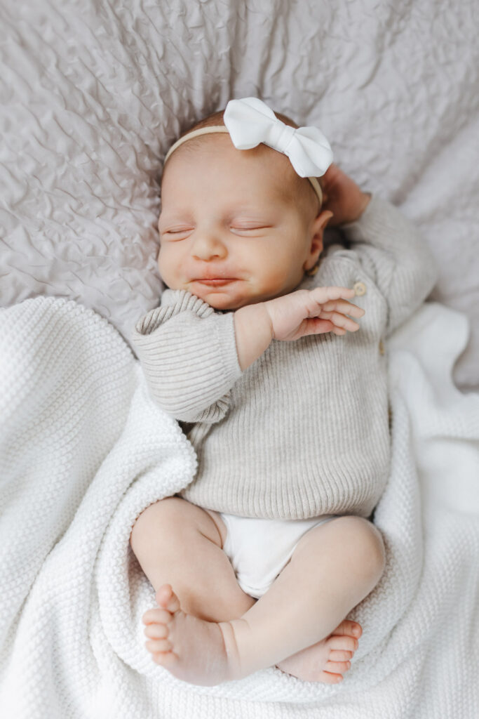 baby girl dressed in neutral knit sweater and white hair bow sleeping during Toronto newborn photo session.
