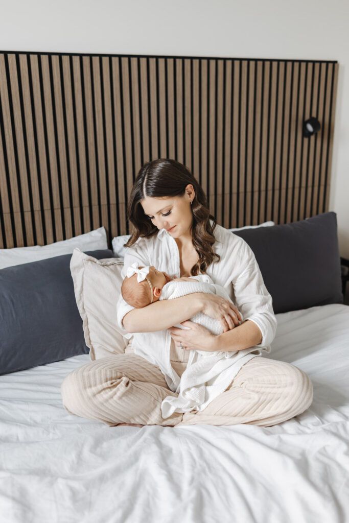Mom dressed in a comfy button up and lounge pants holding her baby girl during at home newborn photography session