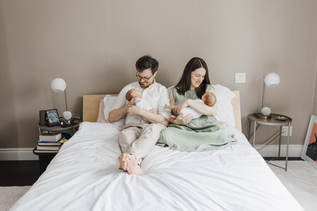 Parents and twin newborns relaxing on bed during toronto newborn photography session